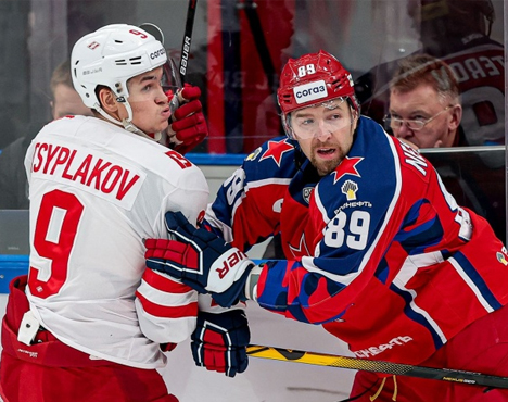 Два хоккеиста в форме команд КХЛ на льду. Один в белой форме с номером 9, другой в синей с номером 89. Они ведут борьбу у борта на фоне стекла, за которым видно судей и зрителей